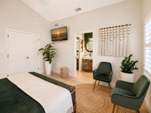 A bedroom with a bed, two chairs, a TV, a plant, and a bathroom visible through an open door. - Sarasota Slice of Paradise (Sarasota)
