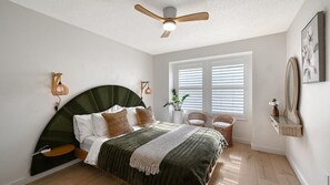 Ein Schlafzimmer mit einem bogenförmigen Bett, einem Deckenventilator, einem Fenster mit Jalousien und einer Wandleuchte.
