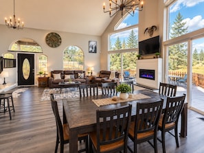 A spacious living room with a fireplace, large windows, and a dining area with wooden furniture. - River Front Getaway! Hot tub & Pool Table. Great location to Sunriver and Bend (Bend)