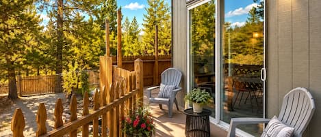 A covered patio with two Adirondack chairs, a wooden fence, and a view of the surrounding trees.