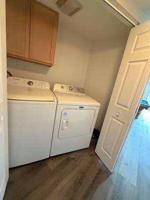 A laundry room with a washing machine and dryer, wooden cabinets above, and a door leading to another room. - River Front Getaway! Hot tub & Pool Table. Great location to Sunriver and Bend (Bend)