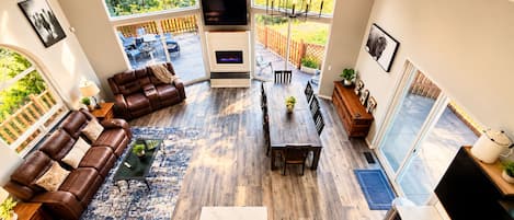 A spacious living area with a fireplace, a large window overlooking a garden, and a dining area with a wooden table and chairs.