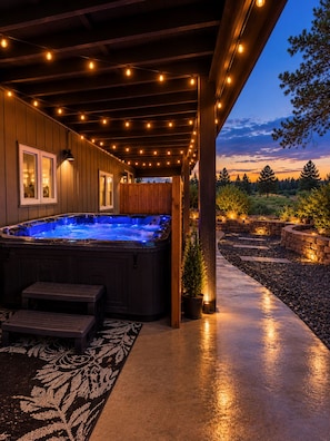 A hot tub under a wooden pergola with string lights, surrounded by a landscaped garden. - River Front Getaway! Hot tub & Pool Table. Great location to Sunriver and Bend (Bend)