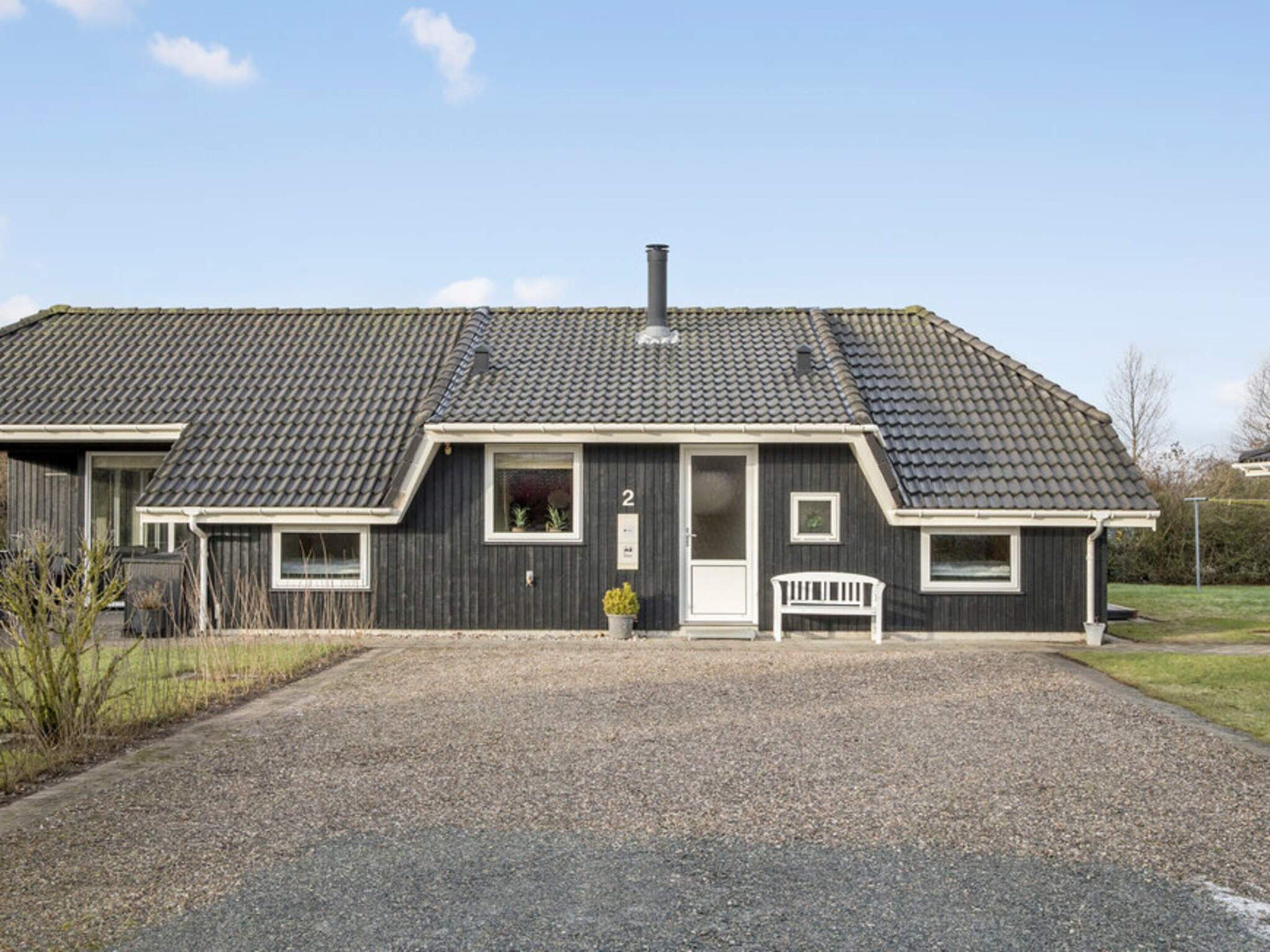 A two-story house with a dark exterior, a chimney, and a gravel driveway.