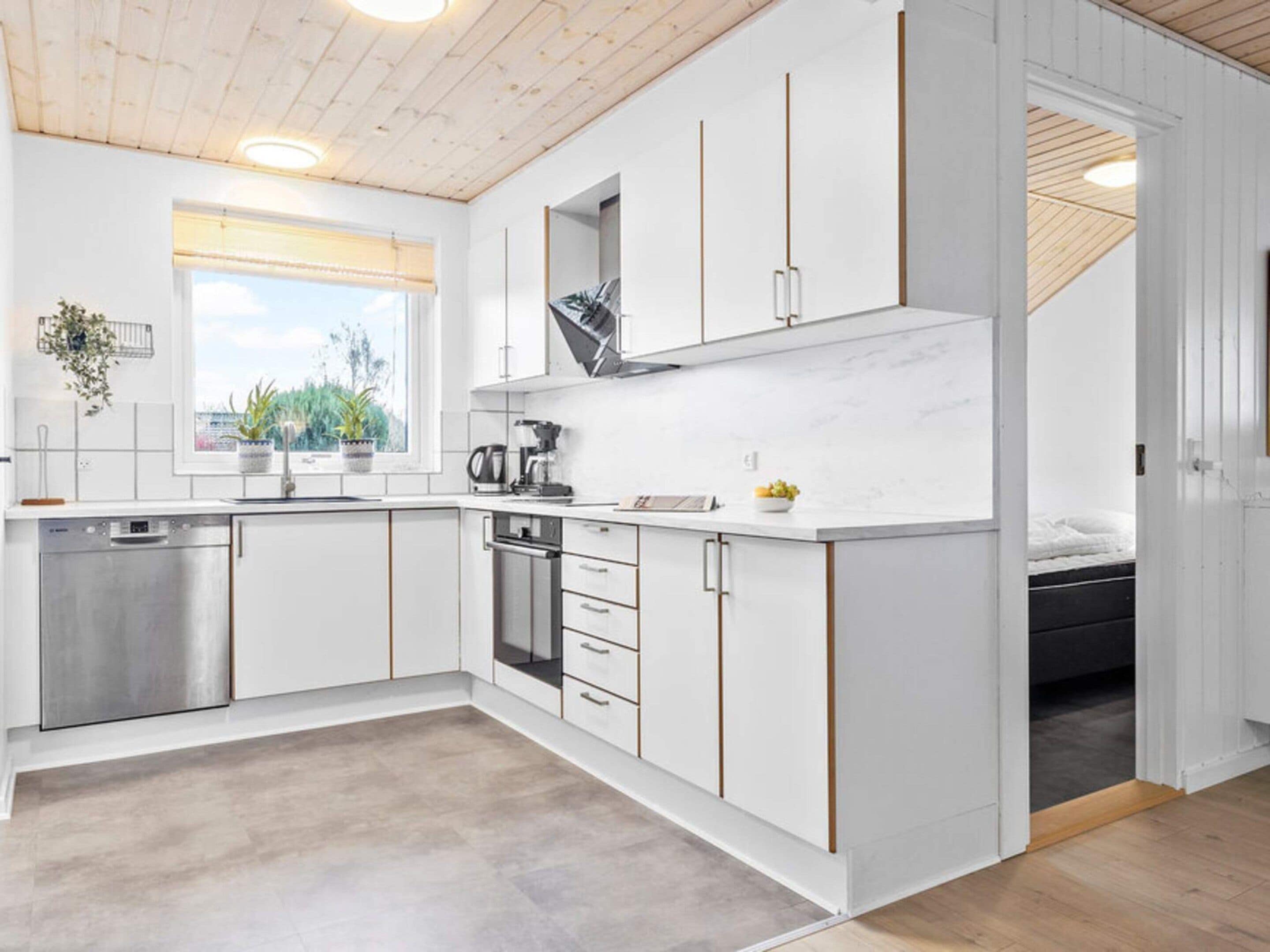 A modern kitchen with white cabinetry, a built-in oven, and a window with a view of greenery.