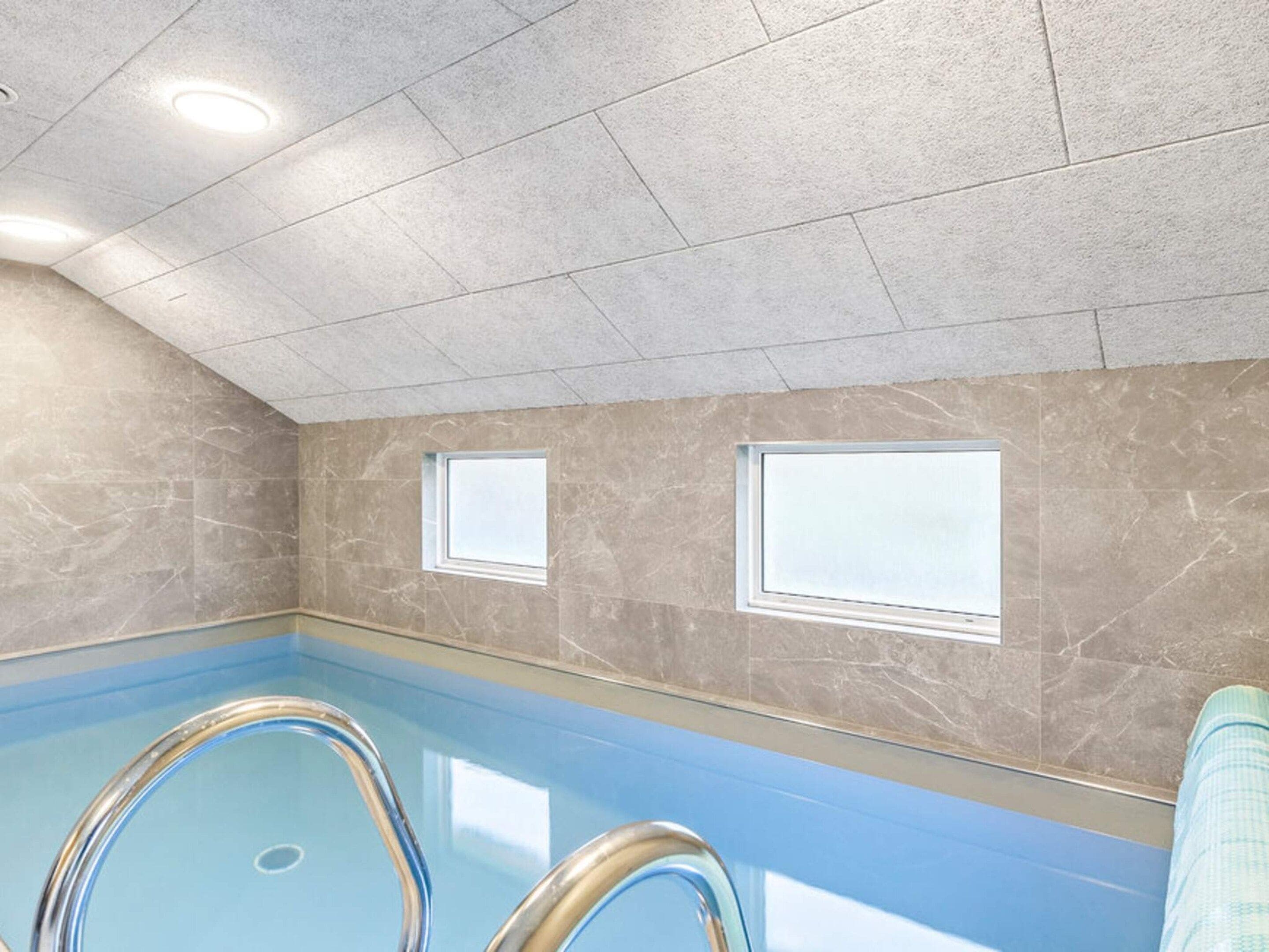 Une piscine intérieure à l’eau claire, avec des murs carrelés et un plafond doté d’un éclairage encastré.