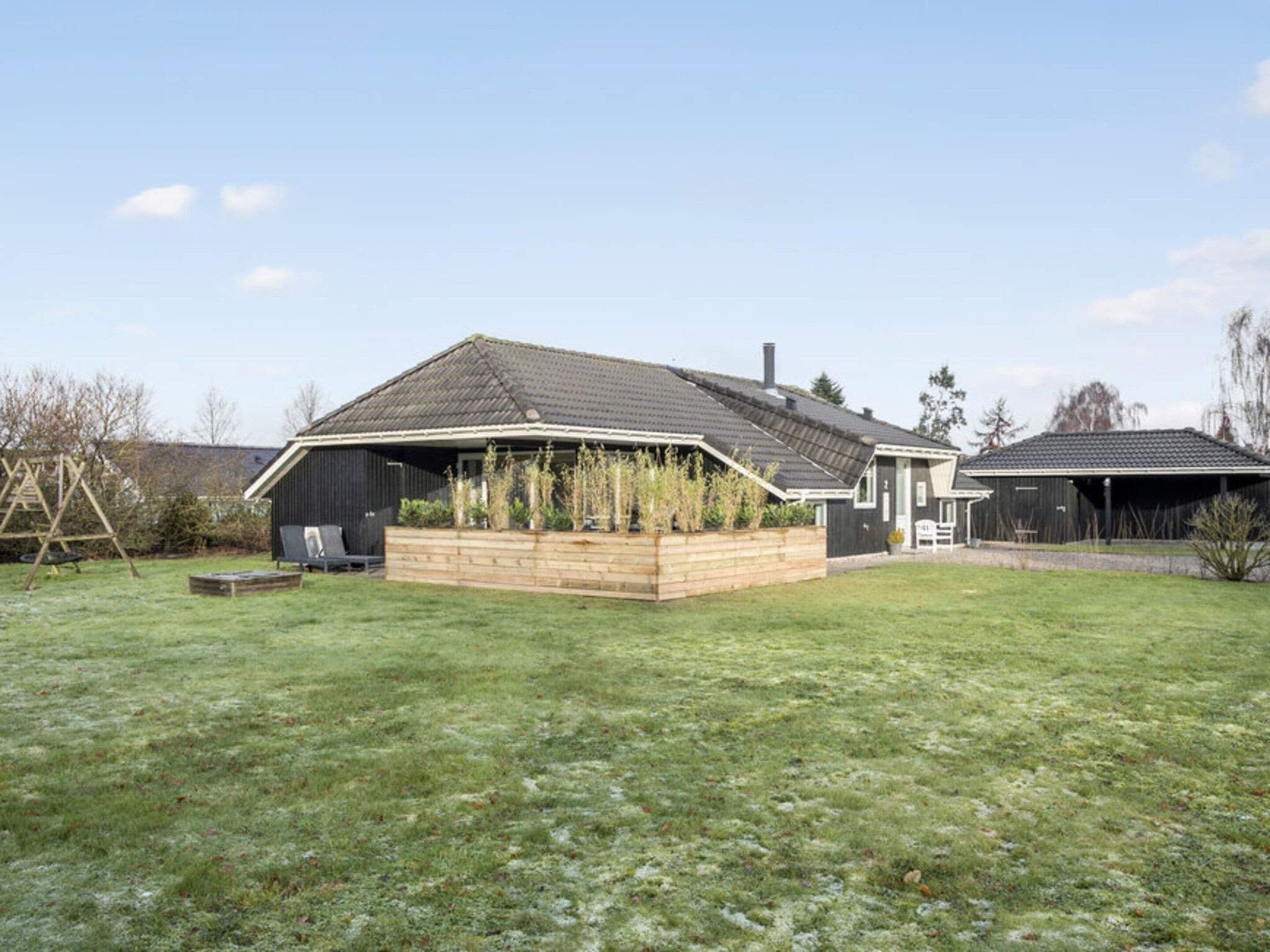 A single-story house with a sloped roof, a wooden deck, and a garden area.