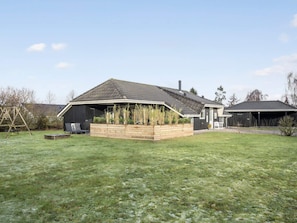 Einbungalow mit geneigtem Dach, einer Holzterrasse und einem Garten.