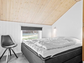 Un dormitorio con techo inclinado, una cama, una silla y un ventanal.