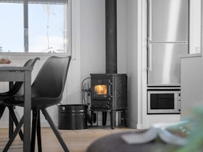 A modern kitchen with a wood-burning stove, a stainless steel refrigerator, and a dining area with chairs and a table.