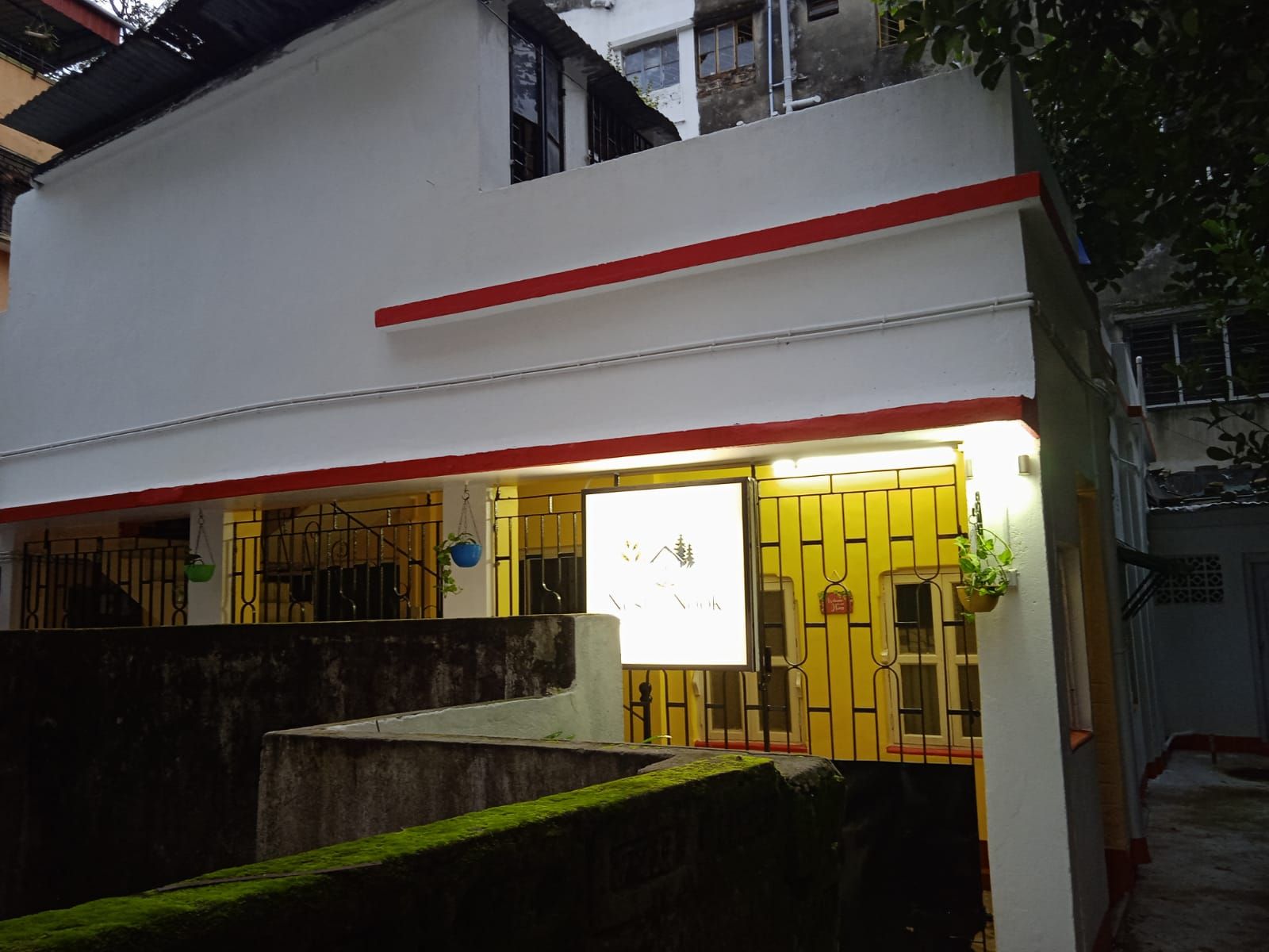 Un edificio con fachada blanca y detalles en rojo, que cuenta con una entrada porticada y un letrero.