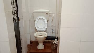 A small, narrow bathroom with a toilet, a visible pipe, and a metal grate on the left wall.
