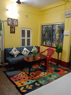 Ein Zimmer mit einer Couch, einem Tisch, einem Sessel, einem gemusterten Teppich und einem Fenster mit schmiedeeisernen Gitterstäben.