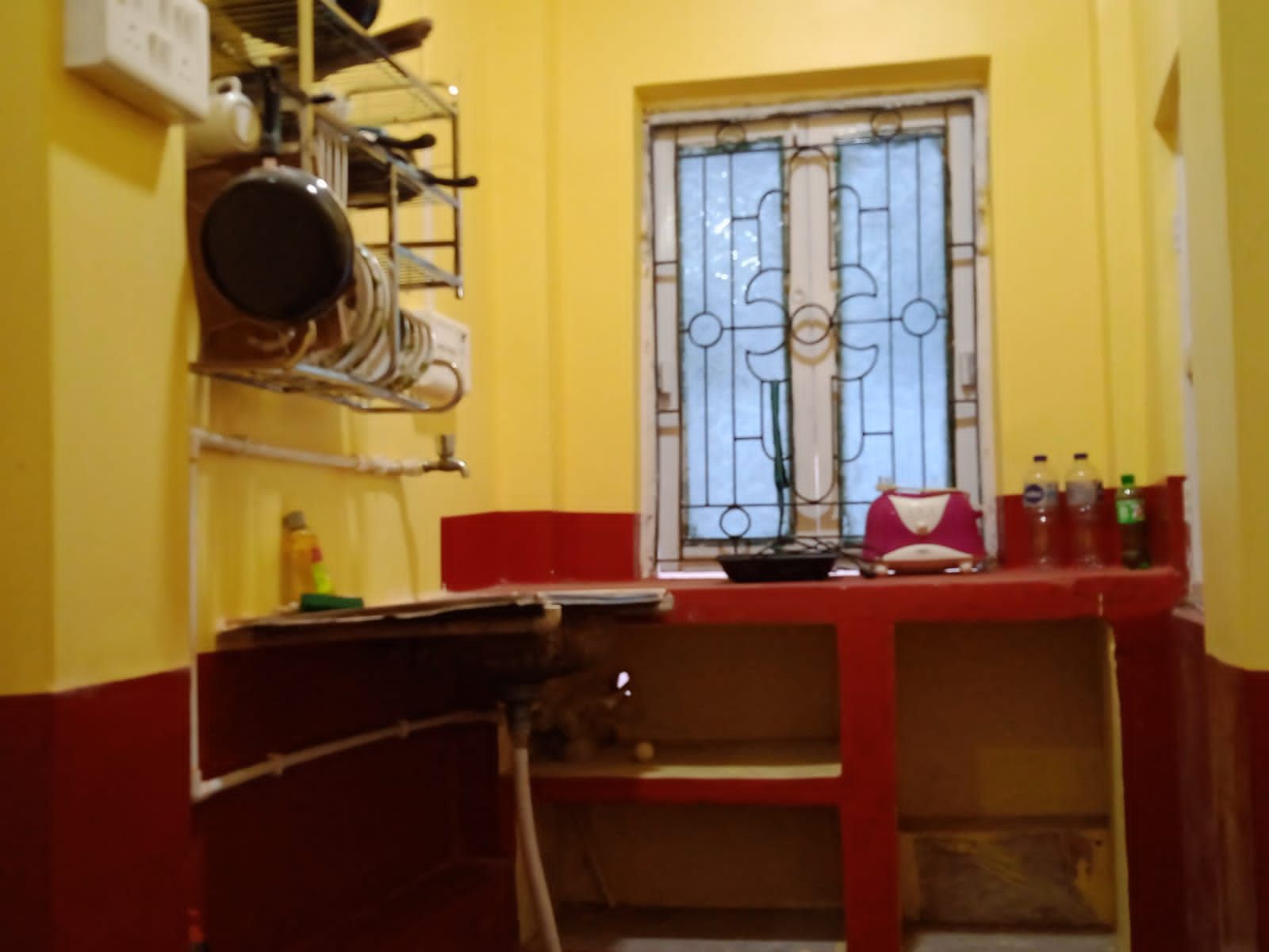 A narrow kitchen with a window, a red countertop, and a metal rack with dishes.