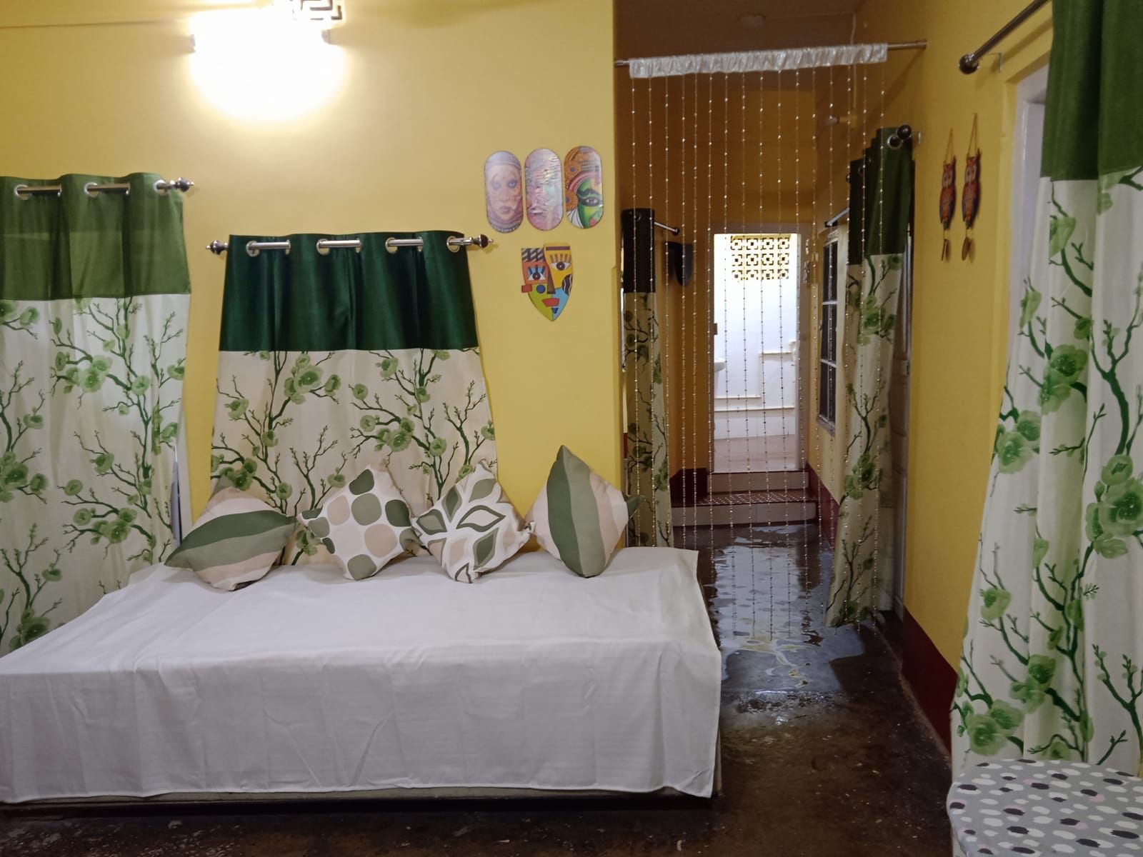 A room with a bed, green curtains, and a hallway leading to a door.
