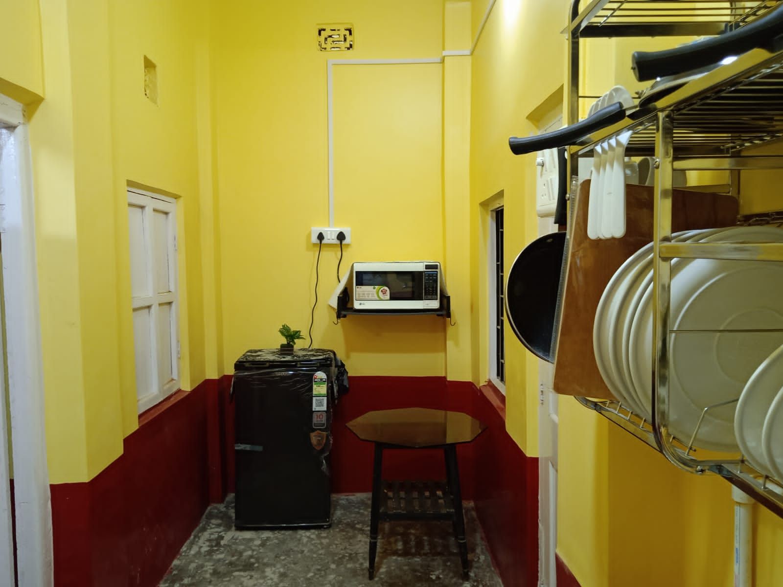 A narrow hallway with yellow walls, a small table, a refrigerator, a microwave, and a water dispenser.
