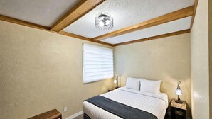 A bedroom with a bed, a nightstand, a bench, a window with blinds, and a ceiling fan. - Ski-to-Door Condo, Kimberley Alpine Resort (Kimberley)