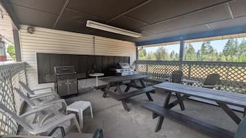 Une terrasse extérieure avec des tables de pique-nique, un barbecue et un espace dédié aux grillades.