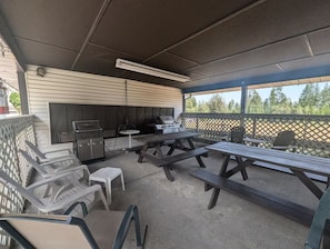 Um pátio externo com mesas de piquenique, churrasqueira e área para churrasco.