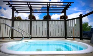 Piscina com pergolado, cercada por um muro branco e vasos de plantas.
