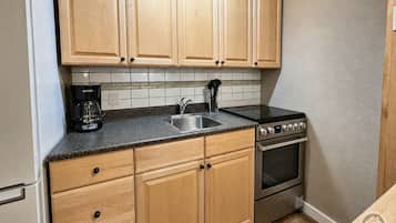 Una cocina con gabinetes de madera, un lavamanos de acero inoxidable, una cafetera y un horno empotrado.