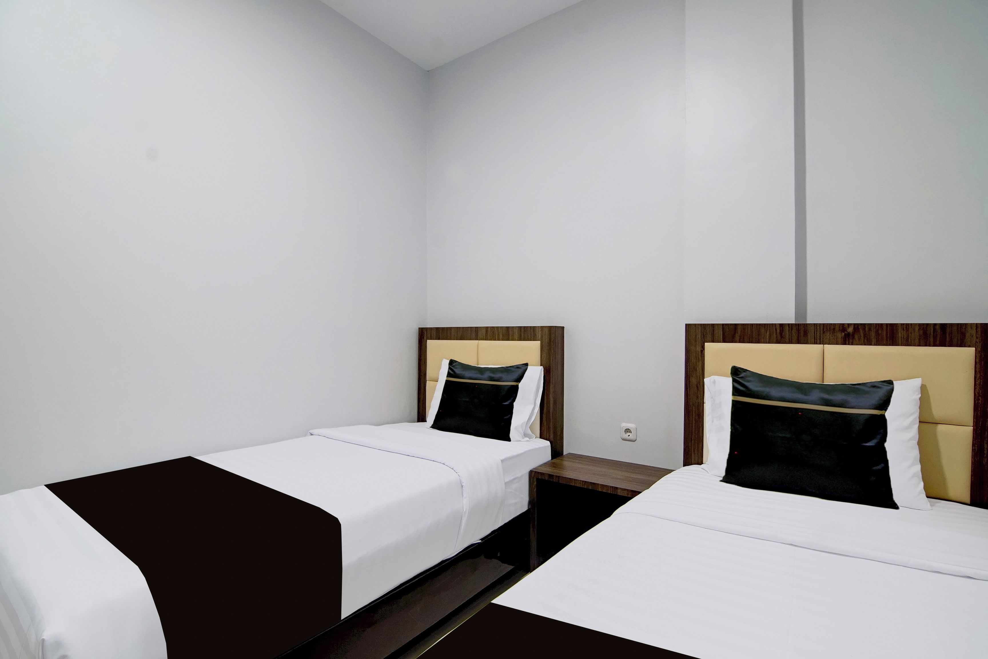 A hotel room with two single beds, each with a wooden headboard and a black and white pillow.