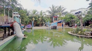 Un parc aquàtic amb tobogan, un edifici petit i palmeres.