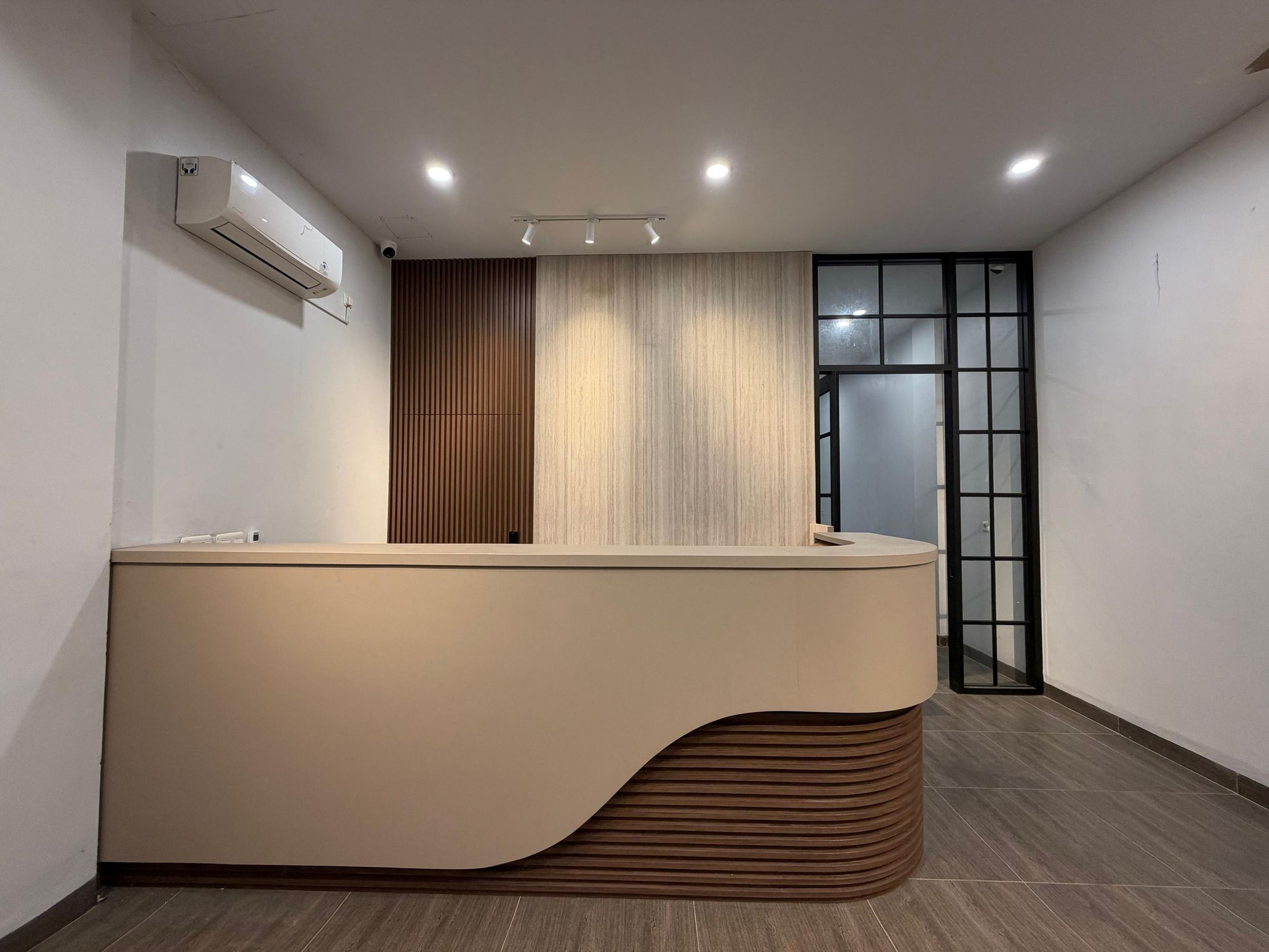 Bancada de recepção com design moderno, ar-condicionado fixado na parede e porta de vidro que dá para outro espaço.