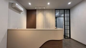 Bancada de recepção com design moderno, ar-condicionado fixado na parede e porta de vidro que dá para outro espaço.