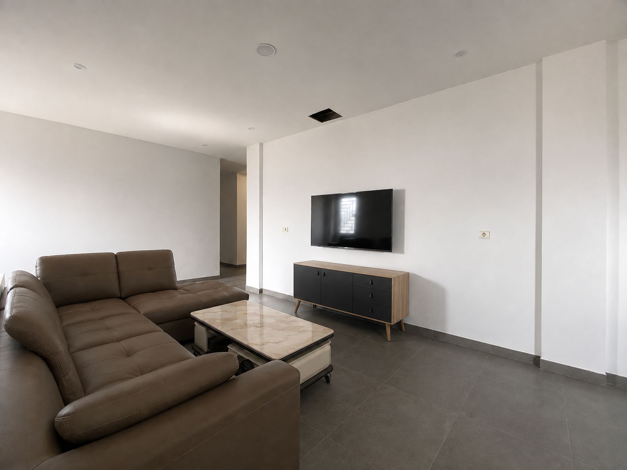 Ein modernes Wohnzimmer mit einem Ecksofa, einem Couchtisch, einem an der Wand montierten Fernseher und einer Holzkommode.