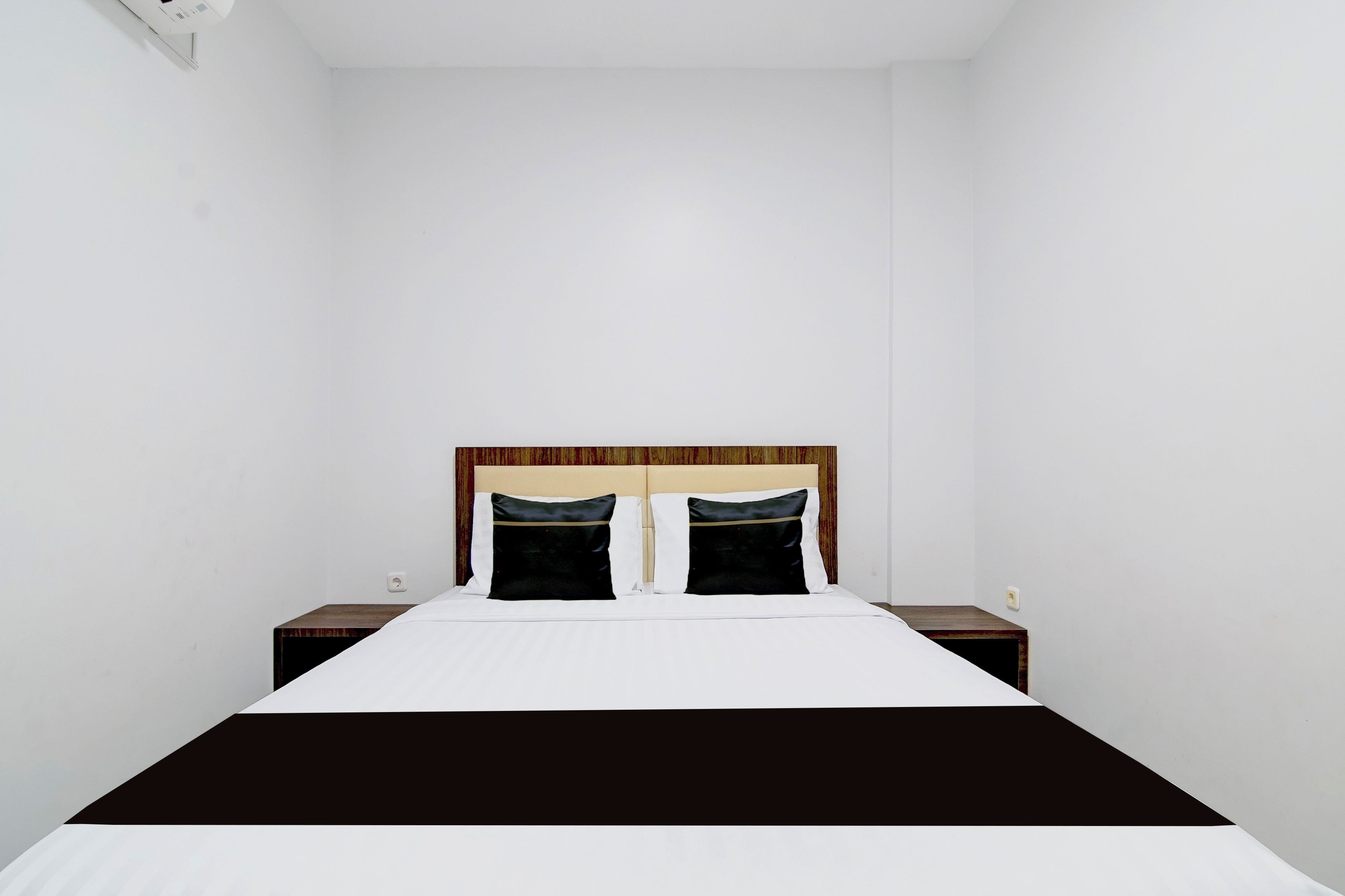 A standard hotel room with a single bed, two bedside tables, and a plain wall.