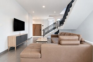 Una sala moderna con un sofá modular, un televisor de pantalla plana y una escalera.