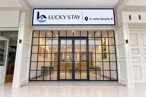 Entrada de un hotel con un letrero que dice 'LUCKY STAY' y un marcador de ubicación que indica 'Jl. Jambu Ujung No. 81'.