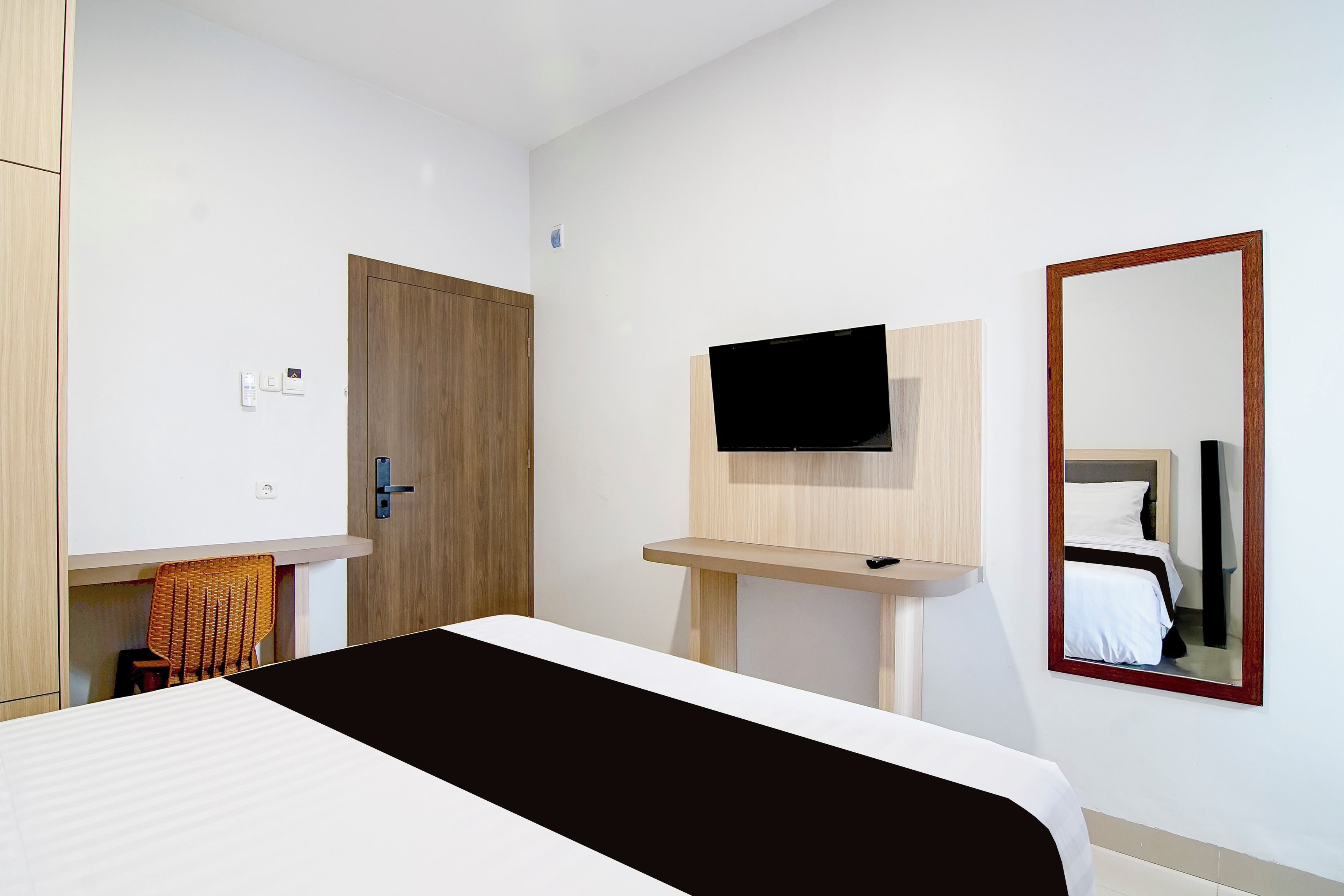 A hotel room with a bed, a television mounted on a wooden stand, a mirror, and a door.