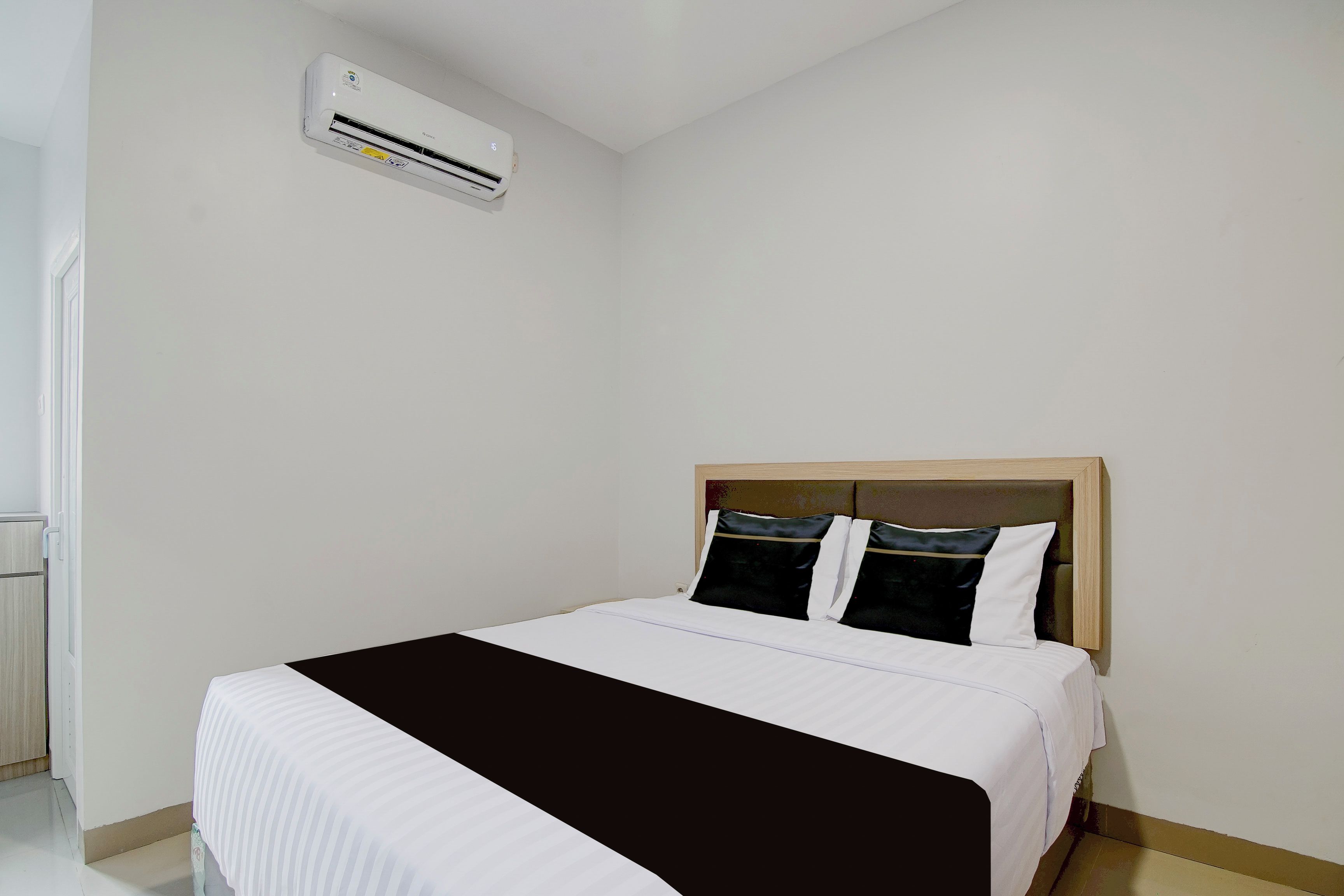 A hotel room with a bed, a headboard, and an air conditioning unit on the wall.