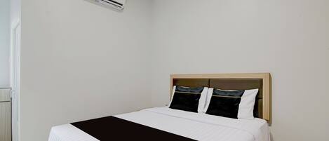 A hotel room with a bed, a headboard, and an air conditioning unit on the wall.