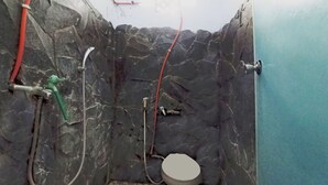 A bathroom with a stone wall, a toilet, and a shower with a green hose. - Collection O near Mall Ciputra (Pekanbaru)