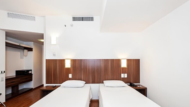 Ein Hotelzimmer mit zwei Einzelbetten, einem Schreibtisch mit Stuhl, einem Kleiderschrank und einem kleinen Nachttisch mit Telefon.