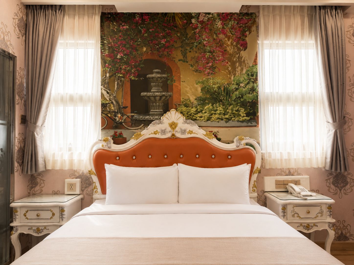 Una cama con un cabecero decorativo, dos mesitas de noche con lámparas y un mural en la pared.