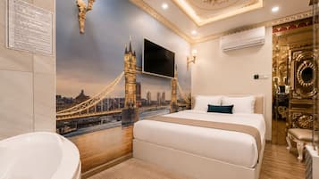 Habitación de hotel con cama, un amplio ventanal con vistas a la ciudad, televisor montado en la pared y baño con lavamanos y espejo.