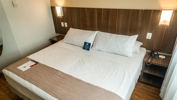 Ein Hotelzimmer mit einem großen Bett, einem hölzernen Kopfteil, Nachttischlampen, einem Telefon und einem Nachttisch.