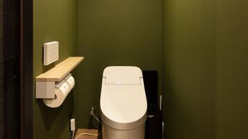 A small, narrow bathroom with a toilet, a paper towel dispenser, and a trash bin.