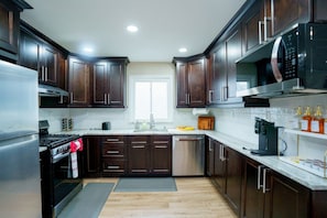 A modern kitchen with dark wood cabinets, stainless steel appliances, and a window providing natural light. - Modern Luxury 3BR | 2 Baths | Parking | Near NYC (Jersey City)