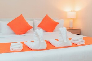 A hotel room with a neatly made bed, orange pillows, and white towels arranged on an orange bedspread. - Modern Luxury 3BR | 2 Baths | Parking | Near NYC (Jersey City)