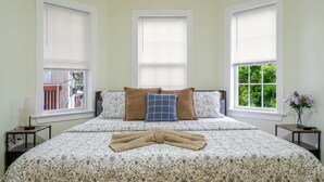 Une chambre à coucher avec un lit double, deux tables de chevet, une lampe et une fenêtre donnant sur un paysage verdoyant.