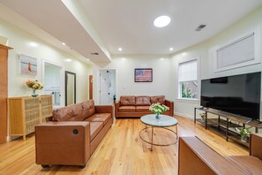 A modern living room with a brown leather sofa, a glass coffee table, a flat-screen TV, and a wooden cabinet.