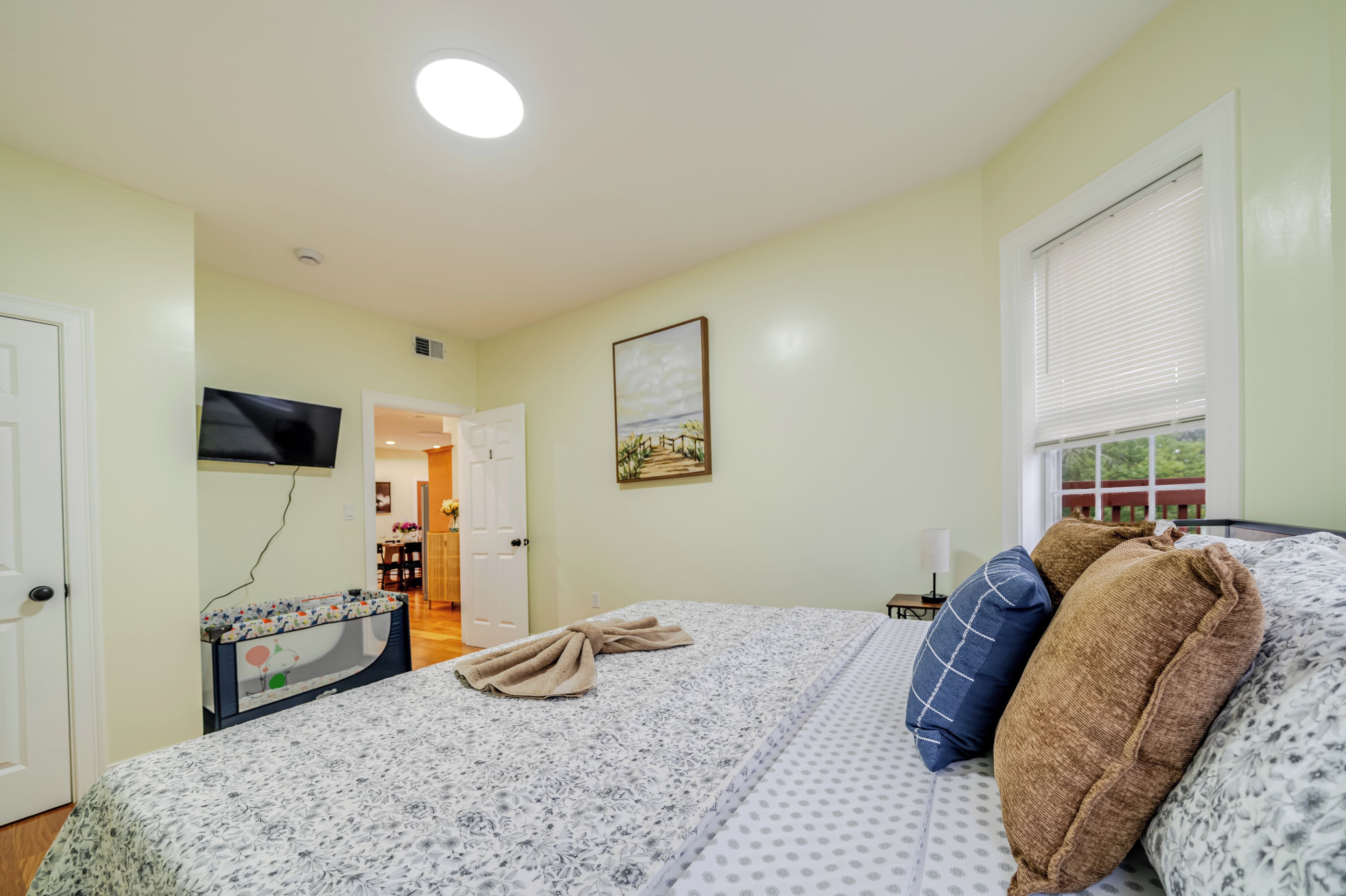 Une chambre à coucher avec un lit, un téléviseur à écran plat, un tableau et une fenêtre avec des stores.
