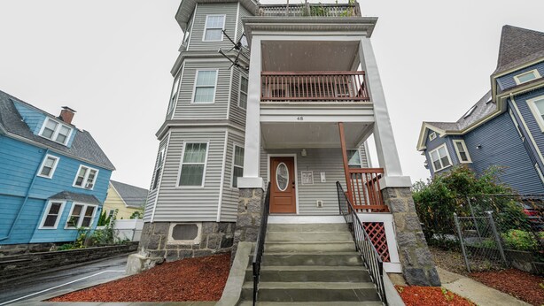 A two-story house with a front porch and a staircase leading to the entrance.