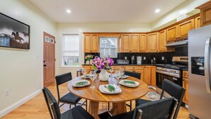 A modern kitchen with wooden cabinets, a stainless steel refrigerator, and a dining area set for six with a round table and black chairs.