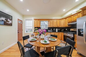 A modern kitchen with wooden cabinets, a stainless steel refrigerator, and a dining area set for six with a round table and black chairs.